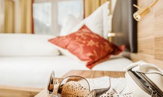 A cozy room view with a white bed and a red pillow. On a table lie a pair of sunglasses and a small bag.