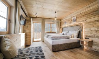 A cozy bedroom with wooden cladding and a large window. The room is bright and modernly furnished, with a comfortable bed and a seating area.