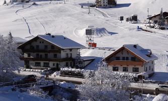 A winter landscape with snow-covered cottages and ski slopes. In the background, mountains and a ski lift can be seen.