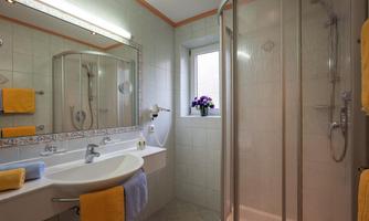 A modern bathroom with a shower and a sink. The walls are light tiled, and the room is decorated with colorful towels.