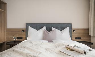A cozy bedroom with a large bed and several pillows. The room has warm wood elements and a soft, inviting atmosphere.