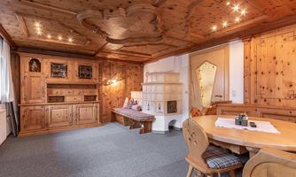 A cozy room with wooden paneling and a rustic fireplace. Wooden chairs are around the table, and the ceiling is artistically designed.