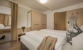 A modern bedroom with two single beds and wooden furniture. The room is bright and inviting, with a window and beautiful decor.