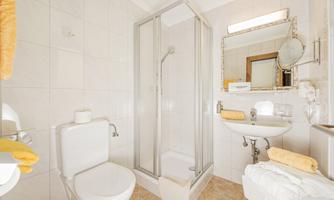 A modern bathroom with a shower, sink, and toilet. The walls are brightly tiled and yellow towels are available.