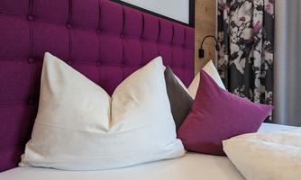 A modern bedroom with a purple headboard and decorative pillows. The surroundings are stylishly and comfortably furnished.