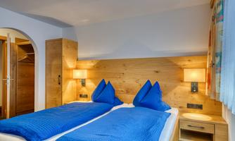 A modern bedroom with two single beds and blue blankets. The walls are made of light wood, and the lighting creates a cozy atmosphere.