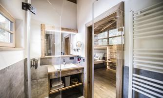 A modern bathroom with a glass shower and wooden shelf. Bright colors and windows create a friendly atmosphere.