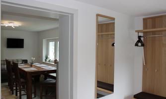 A bright entrance area with a mirror and a sitting place. In the background, there is a dining area with a wooden table and chairs.