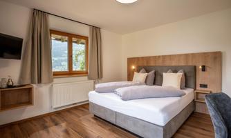 A modern bedroom with a cozy double bed. The room has large windows that let in plenty of light, and a warm wooden surface.