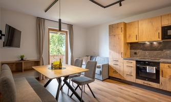 A modern kitchen with wooden cabinets and a dining table. The room is bright and inviting, with large windows that let in natural light.