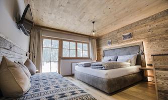 A modern bedroom with wooden decor and a large window. There is a comfortable bed and a relaxing couch.