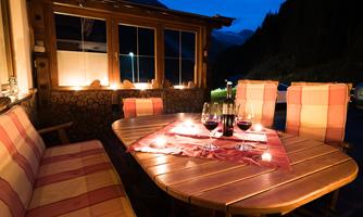 A cozy table with candlelight and wine in a wooden lodge. The view of the mountains in the background creates a relaxed atmosphere at dusk.