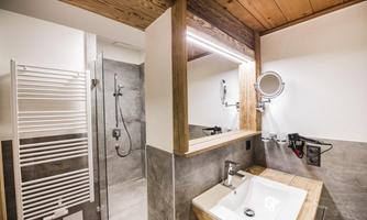 A modern bathroom with wood and concrete accents. There is a shower, a sink, and a large mirror.