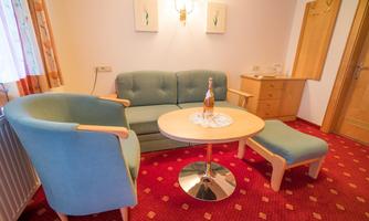 A cozy living area with a green sofa, a round table, and an ottoman. The decor is bright and cheerful with red carpeting.