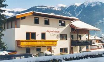 A cozy apartment building in the mountains. The surroundings are covered with snow and there is a clear blue sky.