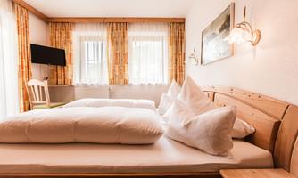 A cozy bedroom with a large bed and two pillows. The windows are bright and provide plenty of daylight, while the walls are decorated with wood.