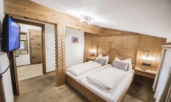 A cozy bedroom with wooden decor and two single beds. The room features a television and soft lighting.