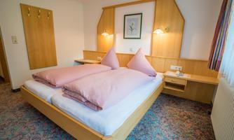 A cozy bedroom with a double bed and two large pillows. The walls are made of wood, and there is a small table as well as a chair in the room.