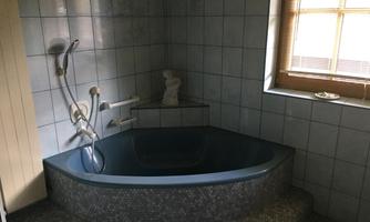 A bathroom with a blue bathtub and tiled walls. There is a window that lets in natural light.