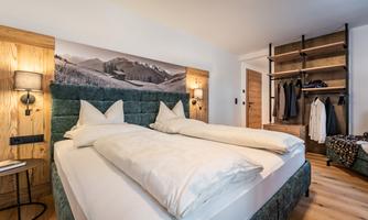 A modern bedroom with a comfortable double bed and soft colors. In the background, there is a beautiful mountain view and an open wardrobe.