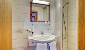 A modern bathroom with white tiles. It includes a shower, a sink, and a mirror.