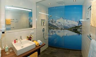 A modern bathroom with a washbasin and a shower. A large wall with a mountain panorama gives the room an inviting atmosphere.