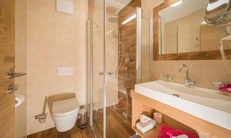 A modern bathroom with wood and tile accents. The shower is separated by a glass panel, and there is a sink with a mirror.