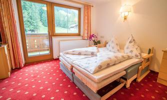 A cozy bedroom with two beds and red carpet flooring. The room features large windows that offer a view of the surrounding nature.