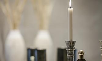 An elegant candle burns in a silver candlestick. Stylish vases and decorative bottles are visible in the background.