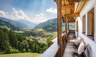 A cozy terrace with a view of a picturesque mountain landscape. The sun shines over the green hills and the village in the valley.
