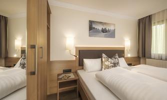 A modern bedroom with two beds and a cozy atmosphere. The walls are painted in light colors, and a piece of artwork hangs above the bed.