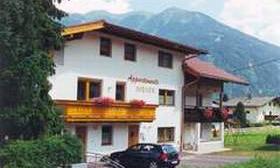 A charming house in the mountains with a balcony and flower boxes. In front of it stands a car, surrounded by green landscape.