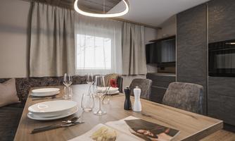 A stylish dining area with a wooden table, set with plates and glasses. Bright curtains and modern light fixtures create a cozy atmosphere.