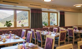 A cozy dining area with wooden tables and elegant chairs. Large windows offer a view of the mountain landscape.