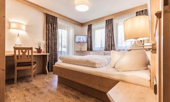 A cozy hotel room with a double bed and a desk. Large window with curtains and a television on the wall.