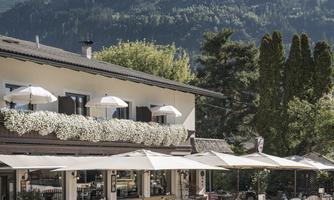 A cozy restaurant with sun umbrellas and blooming plants. In the background, majestic mountains can be seen.