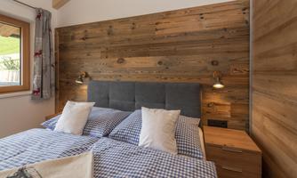 A cozy bedroom with a double bed and checked bedding. The walls are clad in wood, and there are windows with natural light.