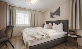 A cozy bedroom with a comfortable bed and modern furniture. Large windows let in plenty of light and create an inviting atmosphere.