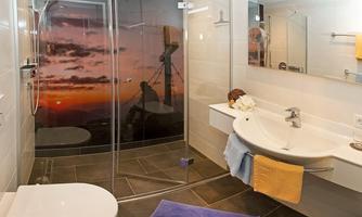 A modern bathroom with a shower and sink. The walls are light, and in the background, a beautiful sunset can be seen.