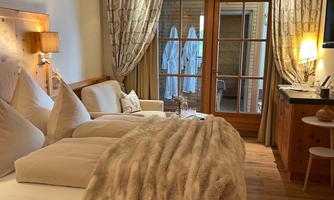 A cozy bedroom with a large bed, a soft blanket, and wooden furniture. Large windows let in plenty of light and create a warm atmosphere.