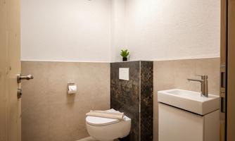 A modern bathroom with a minimalist design. It includes a toilet, a small sink, and decorative plants.