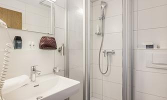 A modern bathroom with a shower and a sink. The walls are tiled in light colors, and there is a large mirror.