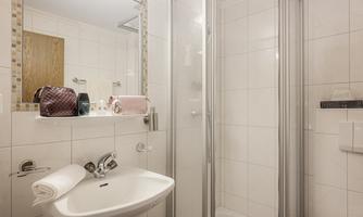 A modern bathroom with a shower, a sink, and bright tiles. On the shelf, there are cosmetic bags and towels.