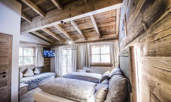 A cozy bedroom with a wooden ceiling and two beds. There is a window with a view outside and a television on the wall.