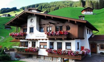 A traditional alpine house with flower boxes. The surrounding landscape is green and hilly.