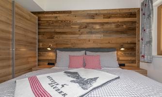 A cozy bedroom with a wooden panel wall design and a comfortable bed. The red and gray pillows as well as the blanket give the room an inviting atmosphere.