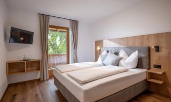 A modern bedroom with two separate beds and elegant wood paneling. Through the window, a lot of natural light shines in and a green view is visible.