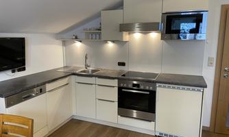 A modern kitchen with bright cabinets and an elegant dark workspace. It is equipped with a stove, a microwave, and a sink.