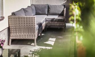 A cozy seating area made of rattan with gray cushions, ideal for relaxed hours outdoors. Surrounded by plants on a sunny balcony.
