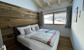 A cozy bedroom with a double bed and wood paneling. The view through the window shows a winter landscape.